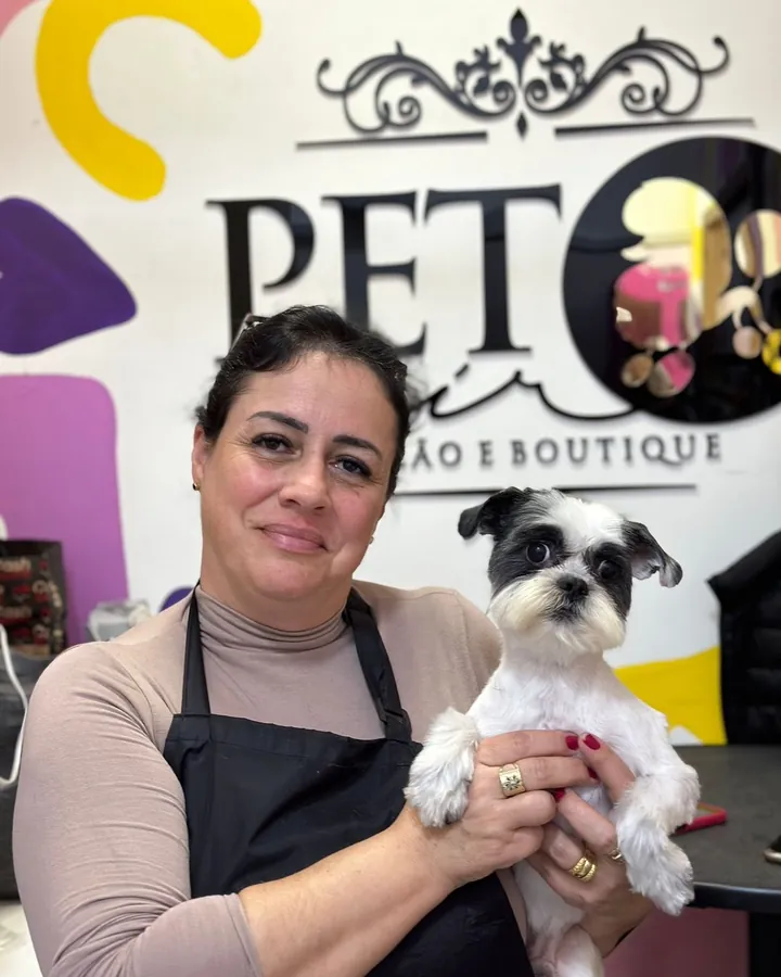 Aluna de avental segurando um shih-tzu preto e branco em frente ao letreiro do Pet Hair