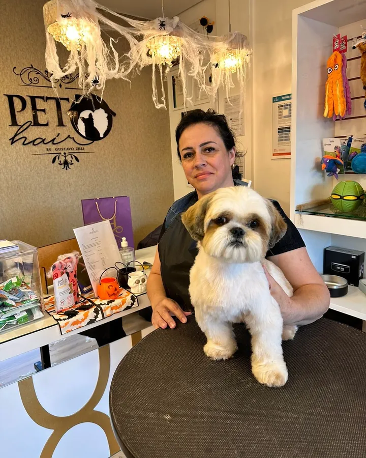 Aluna na recepção do salão com um shih-tzu de pelo aparado sobre a mesa