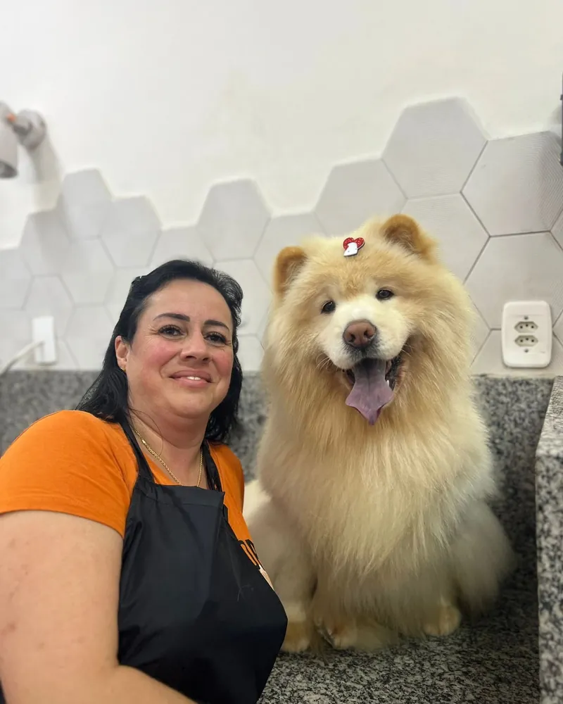 Aluna de avental ao lado de um chow-chow de pelagem clara e volumosa, depois do banho